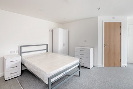 A studio room in 59 West Street. On the left hand side is a bed side table, double bed, wardbrobe and chest of drawers. On the right hand side is a door.